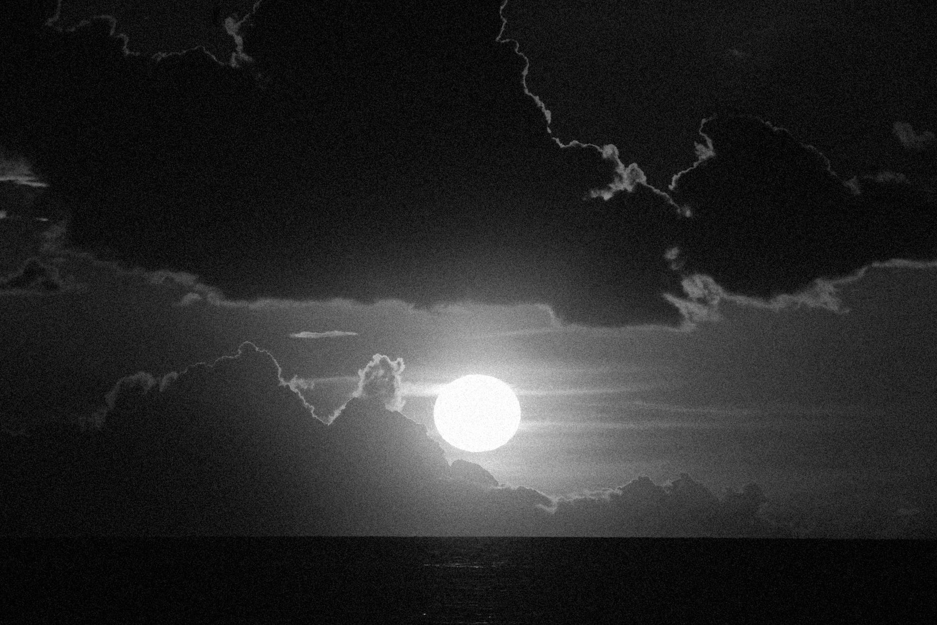 A captivating black and white image of the moon surrounded by dramatic clouds at night.