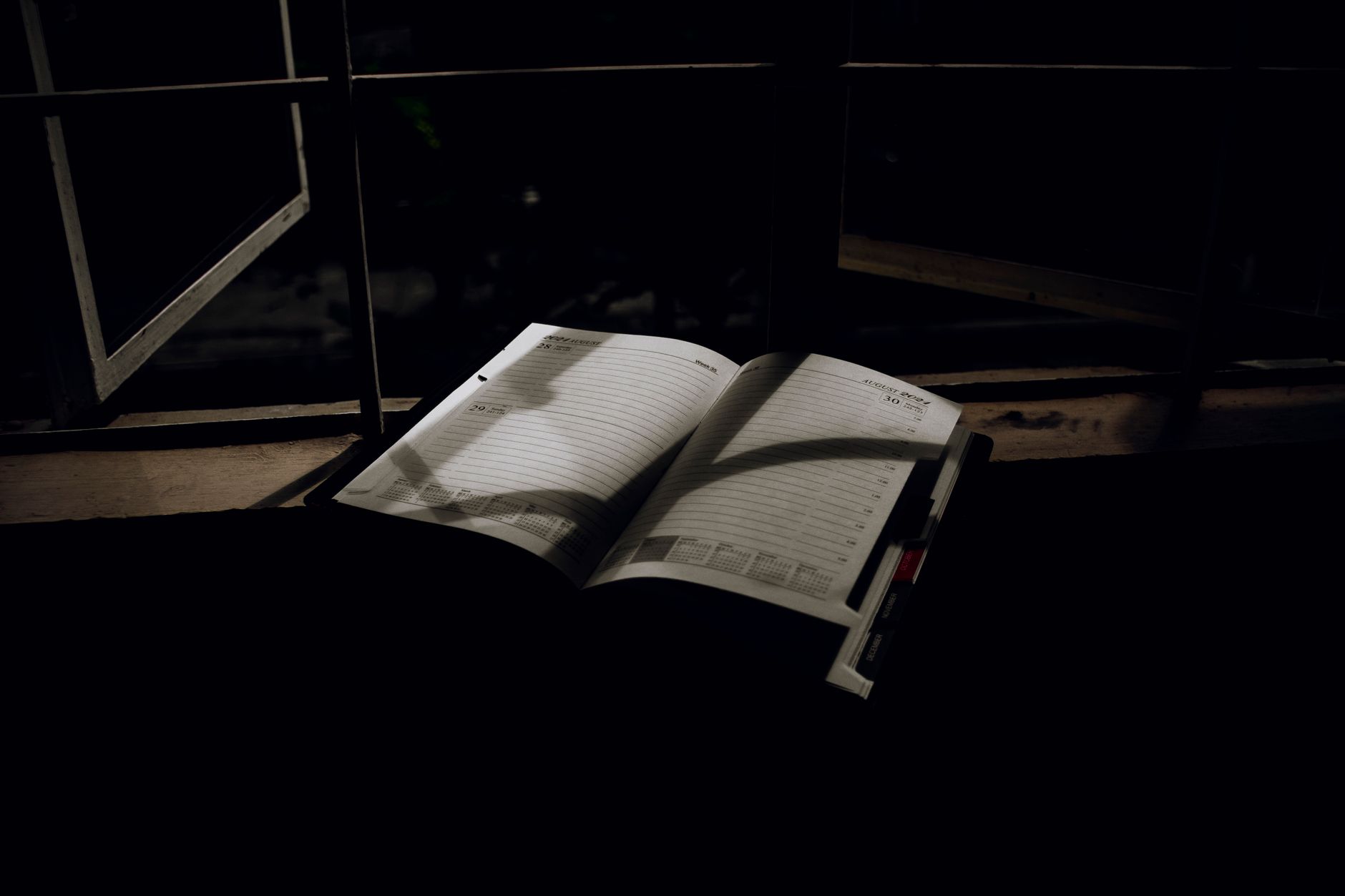 An open planner with dramatic lighting sits on a window sill at night. Ideal for creative projects.