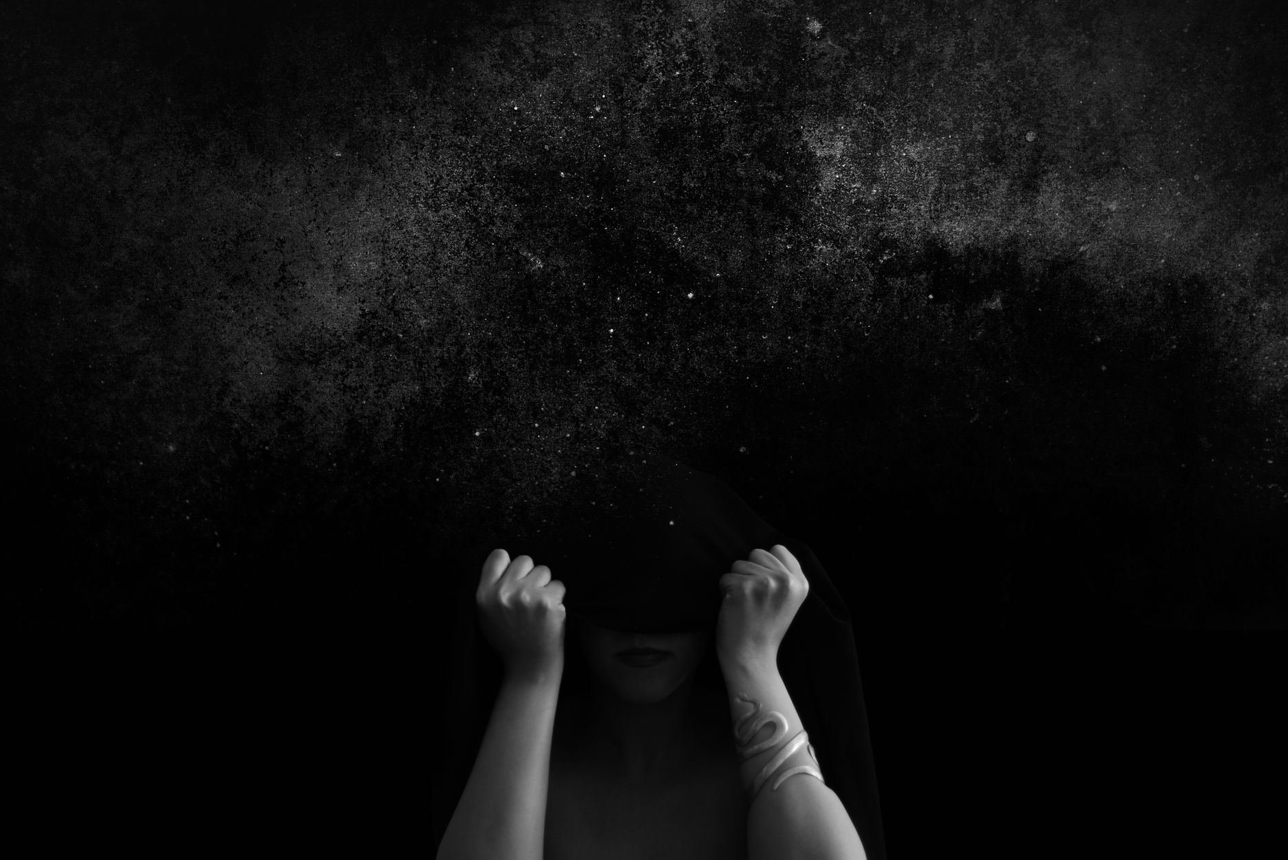 A mystical black and white image of a person obscured beneath a textured sky, evoking intrigue and contemplation.